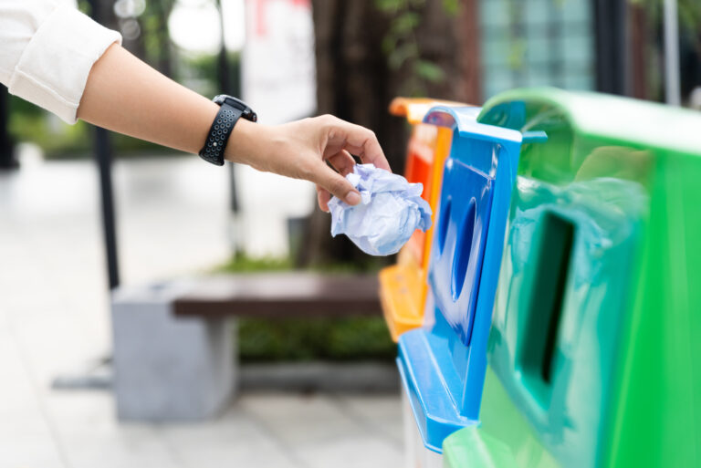a photo for the blog post 10 ways to reduce your carbon footprint, someone putting recycling into a recycling bin