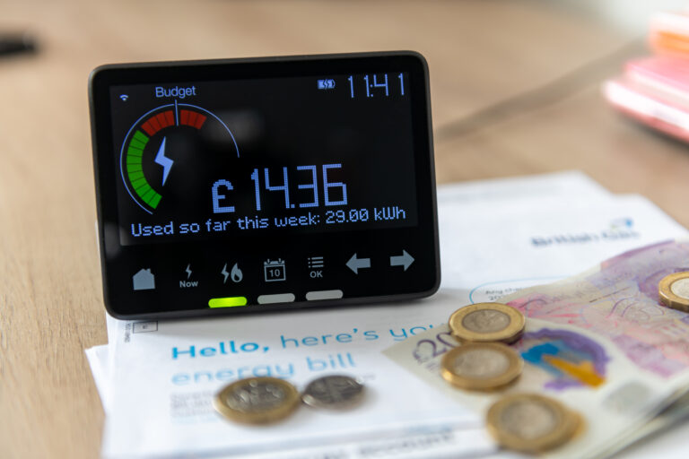 A smart meter above electricity bills on a table to showcase the October 2025 price cap